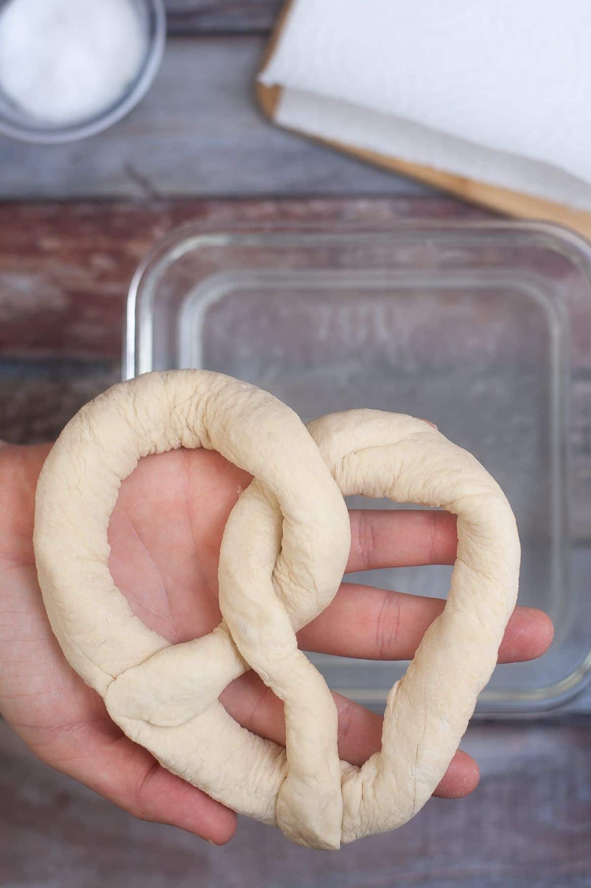 The pretzel dough is being held by a hand. 