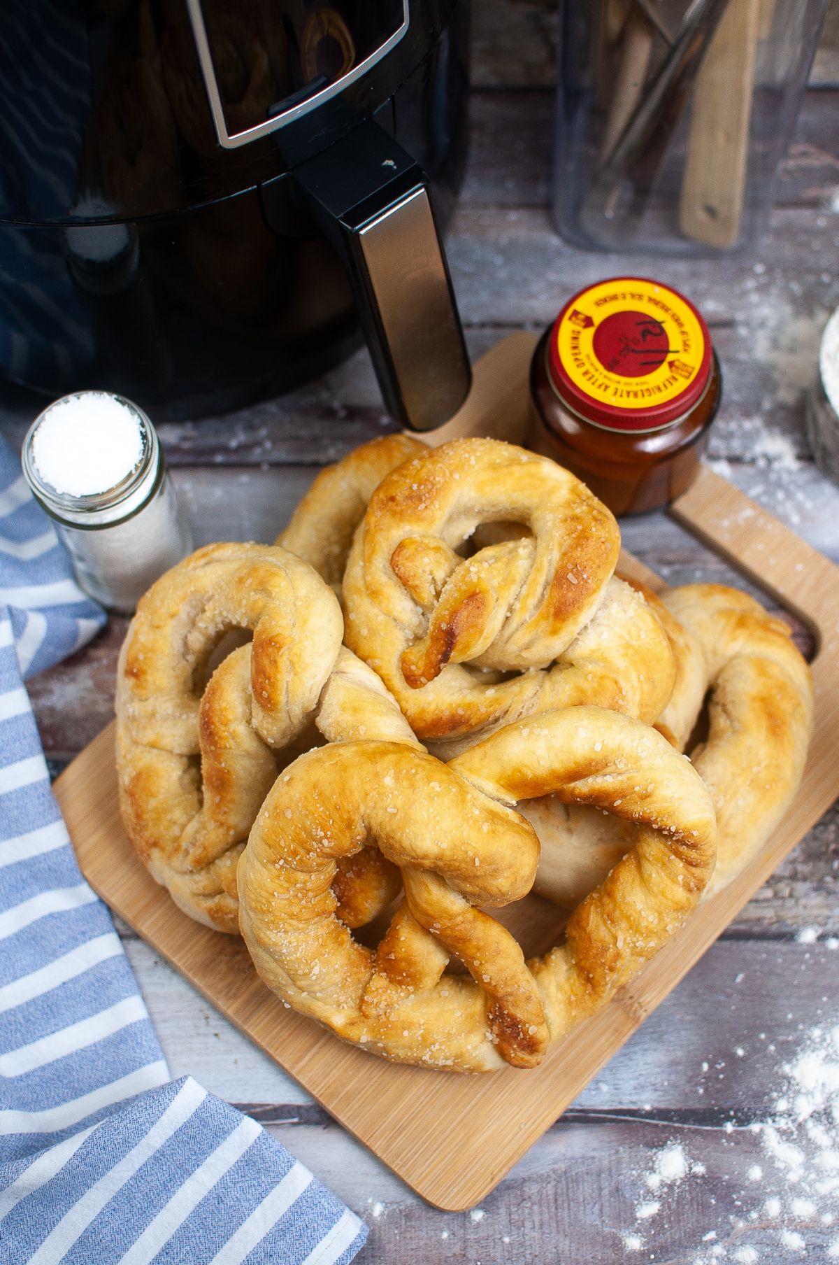 Pretzels Copycat Auntie Anne's Recipe on a wooden chopping board with Air Fryer, salt and sauce on the side.