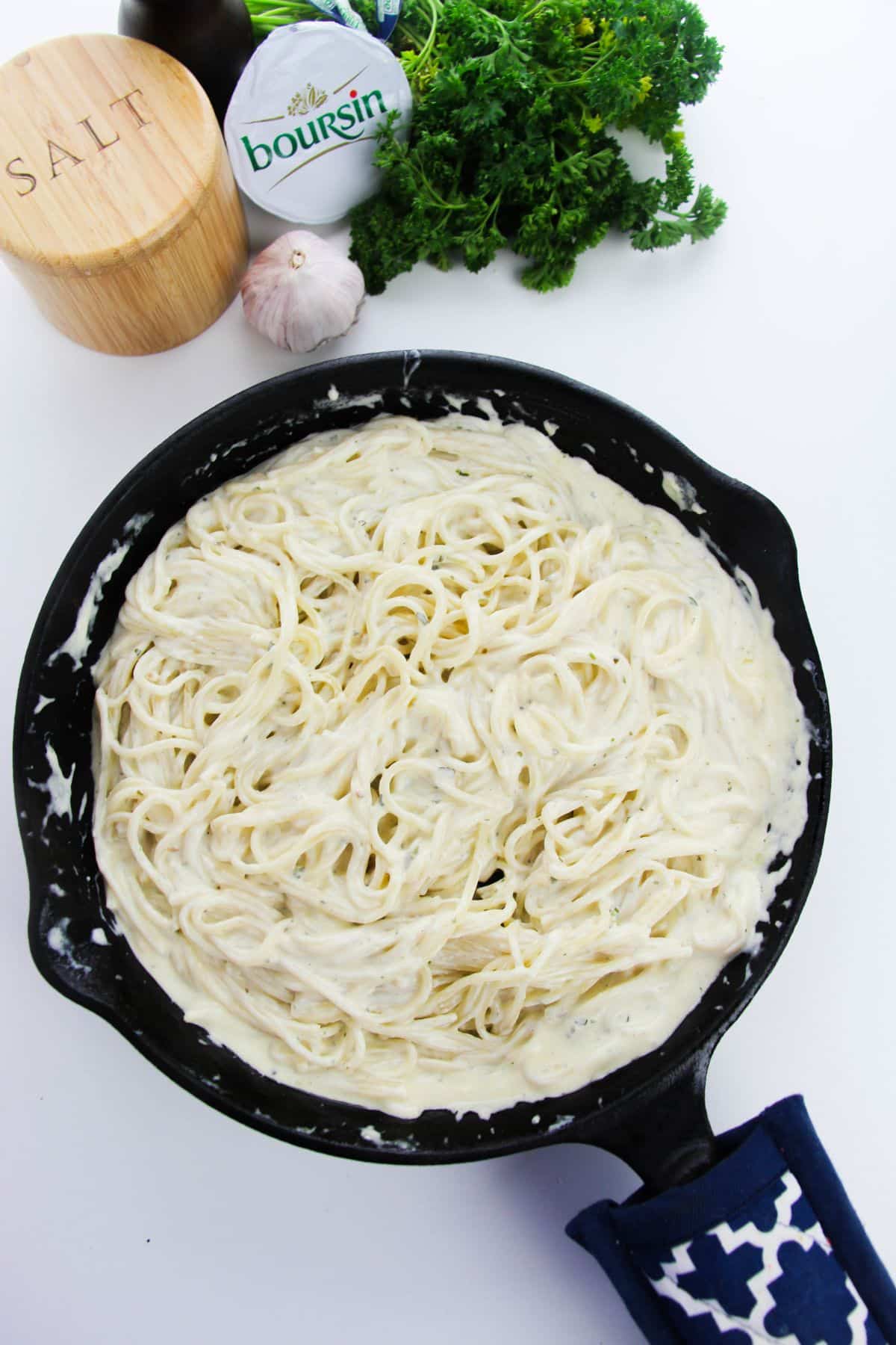 Pasta with cheese mixture in a skillet with ingredients on the side.