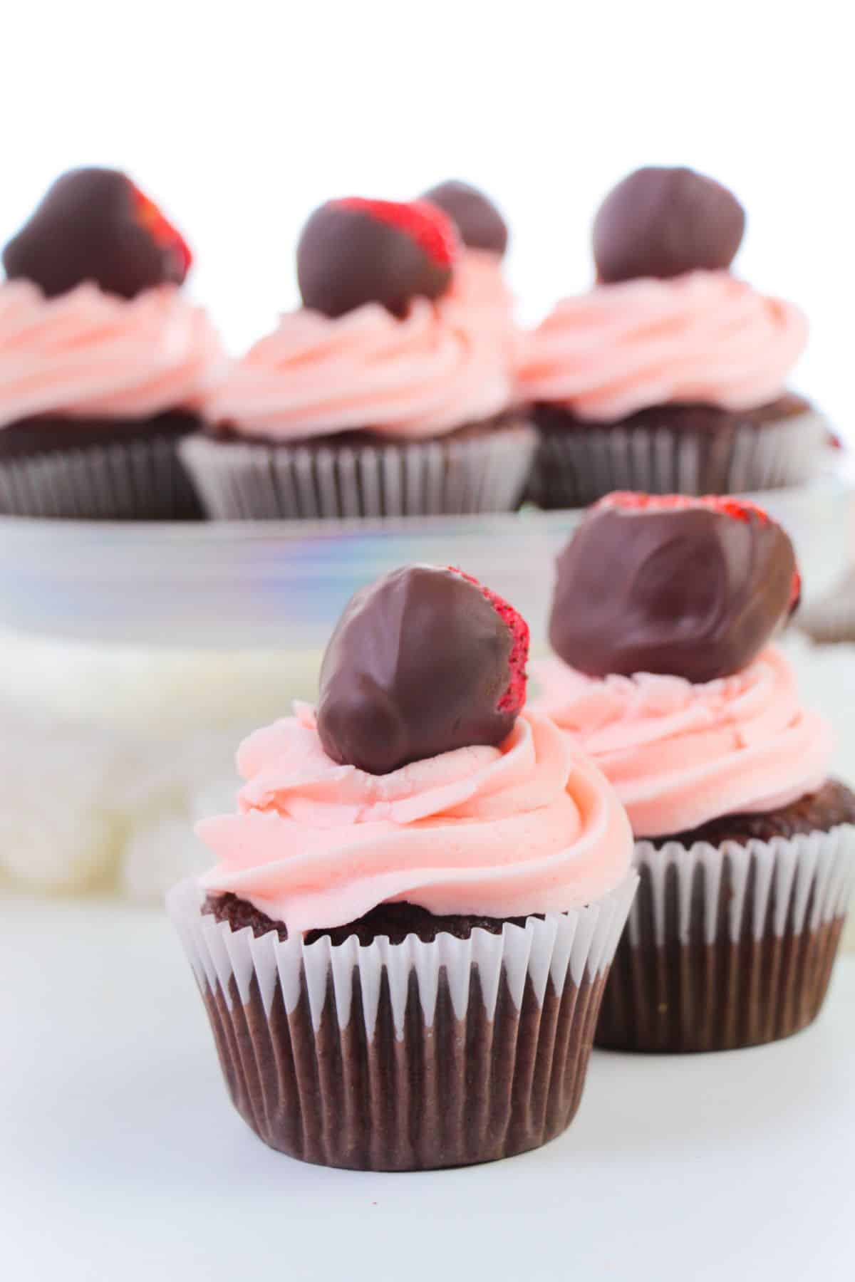 2 Chocolate Strawberry Cupcakes with more cupcakes blurred in the background.