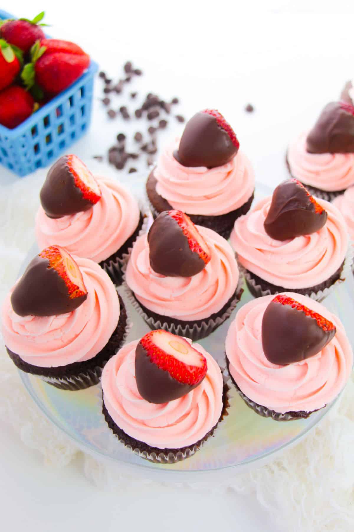 Chocolate Strawberry Cupcakes on a serving plate, with strawberries and chocolates on the side.