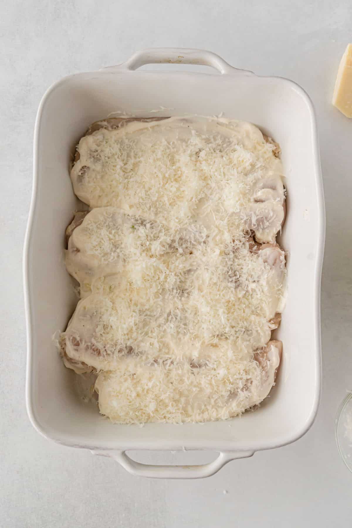 chicken in a baking dish topped with mayo mixture and parmesan cheese.