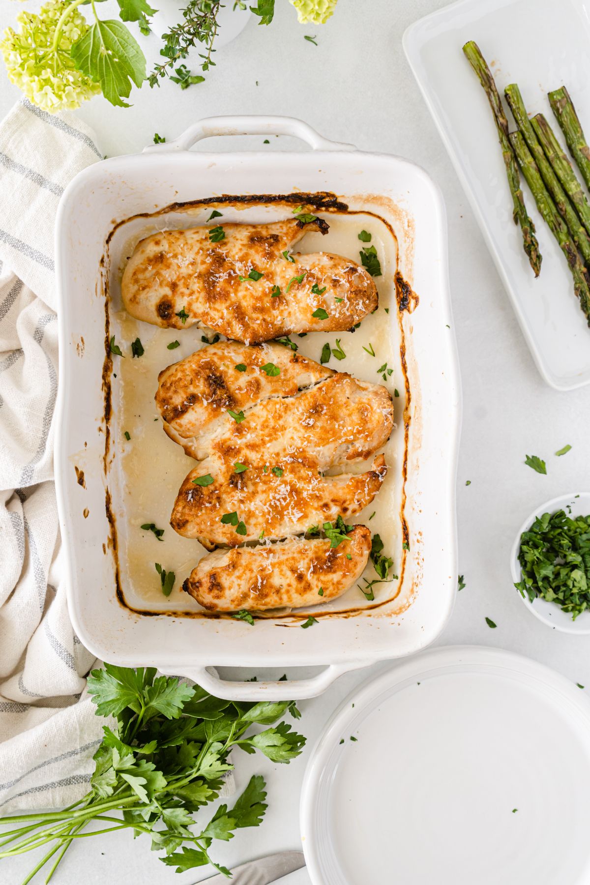 Mayo Parmesan Chicken in a baking dish with asparagus and salad on the side.