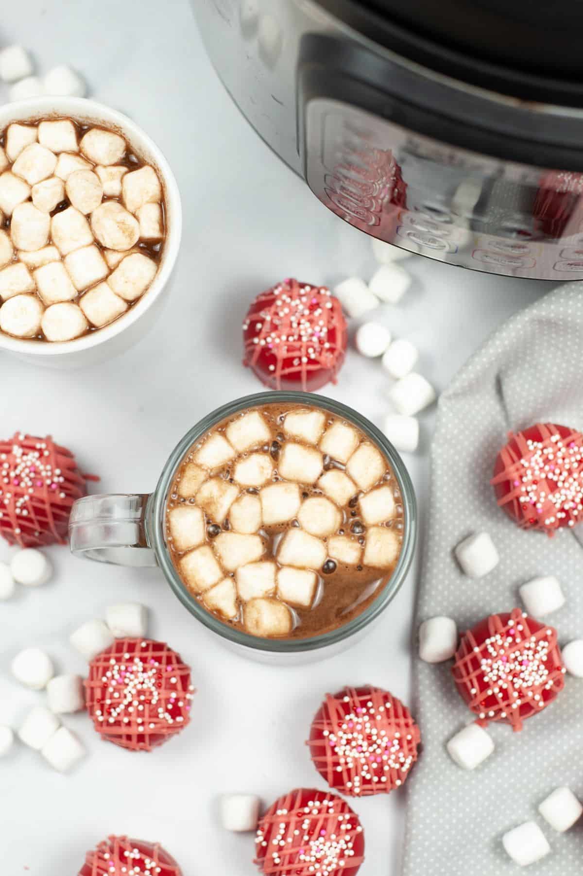hot chocolate in a mug next to Valentine cocoa bombs and marshmallows.