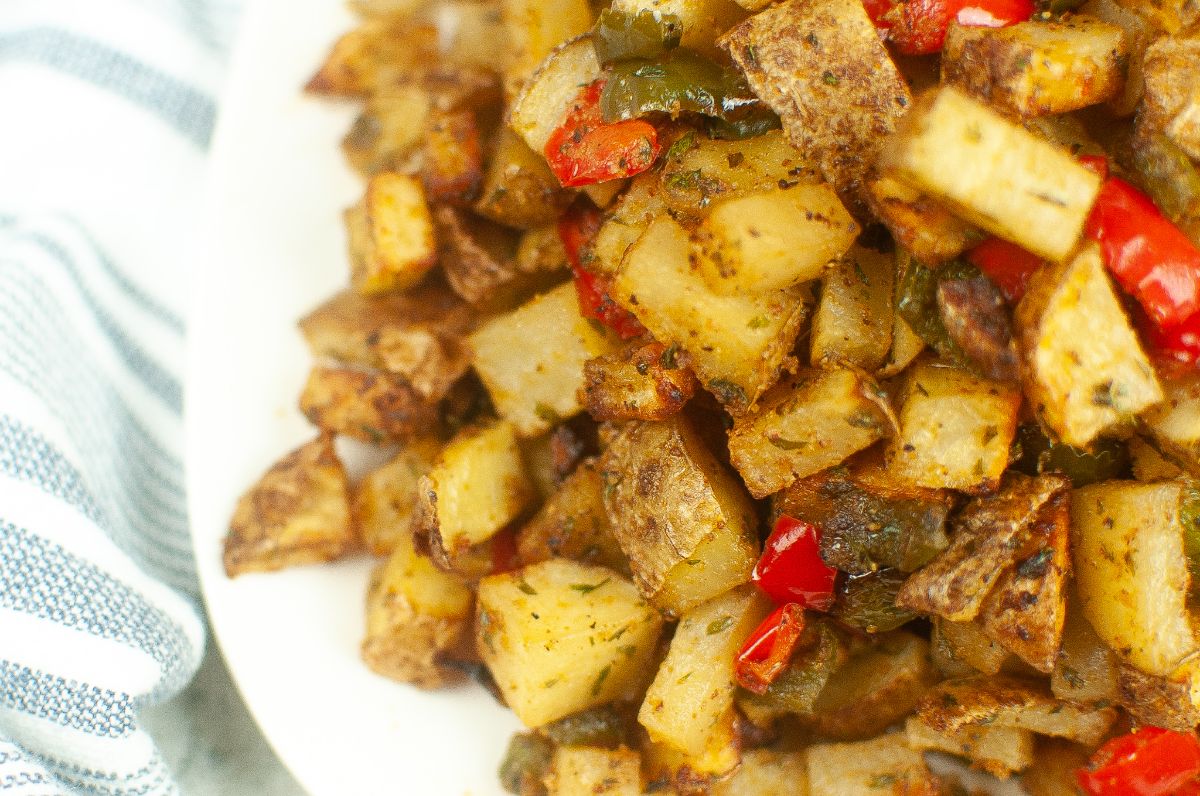 A close up of air fryer breakfast potatoes on a white plate next to a striped cloth.