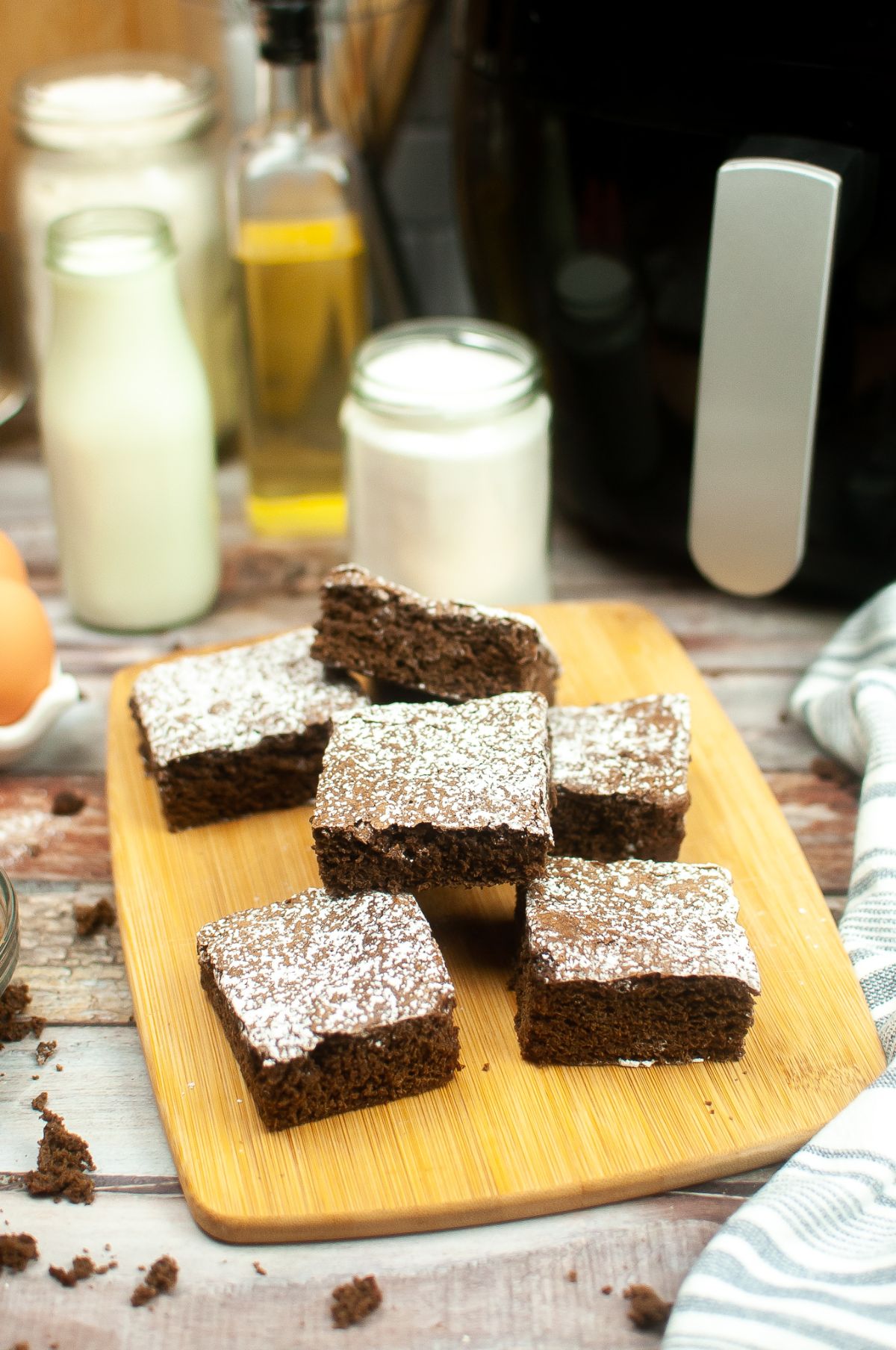 Air Fryer Brownies on a wooden chopping board. Air Fryer and other ingredients on the side.