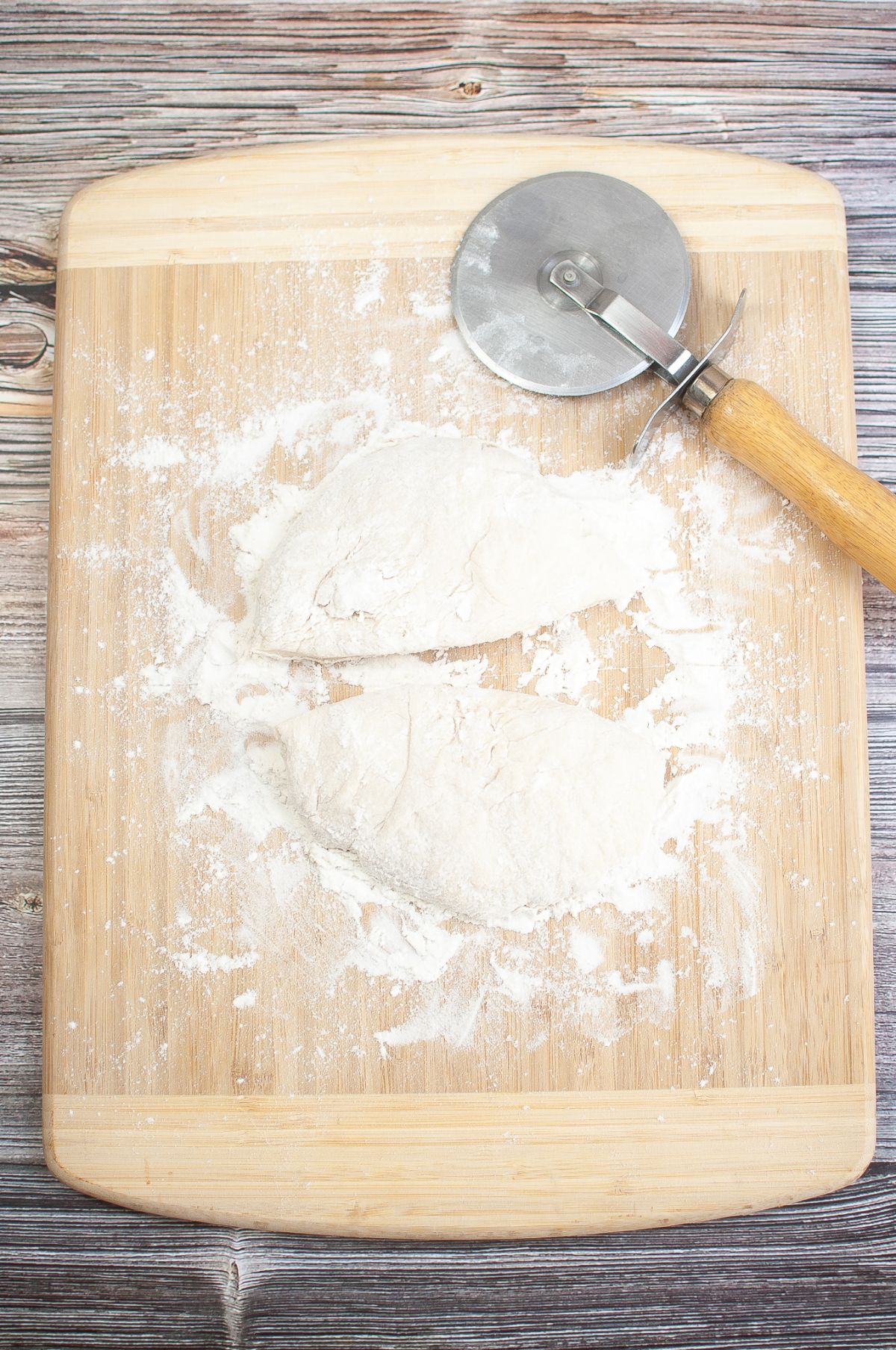 Dough ball divided in two on a wooden board with rolling cutter on the side.