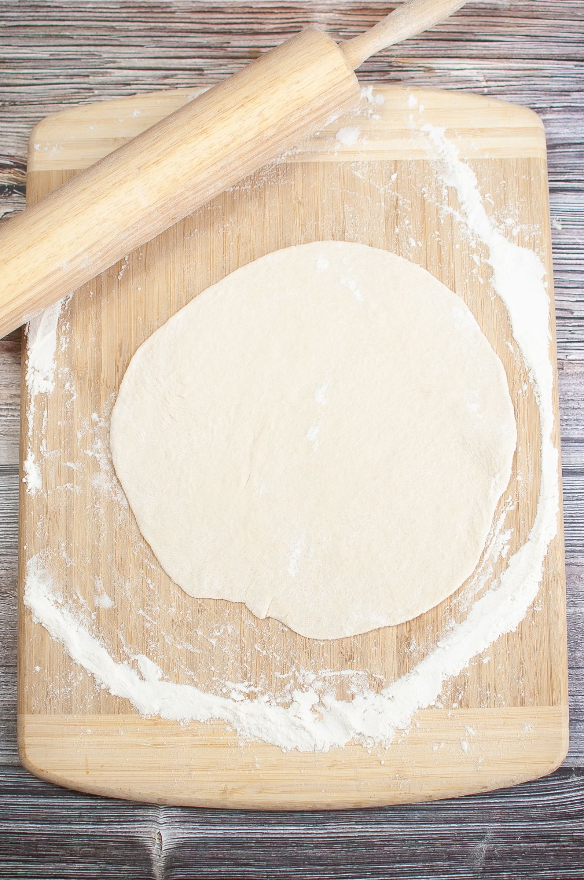 Rolled out dough on a wooden chopping board with rolling pin on the side.