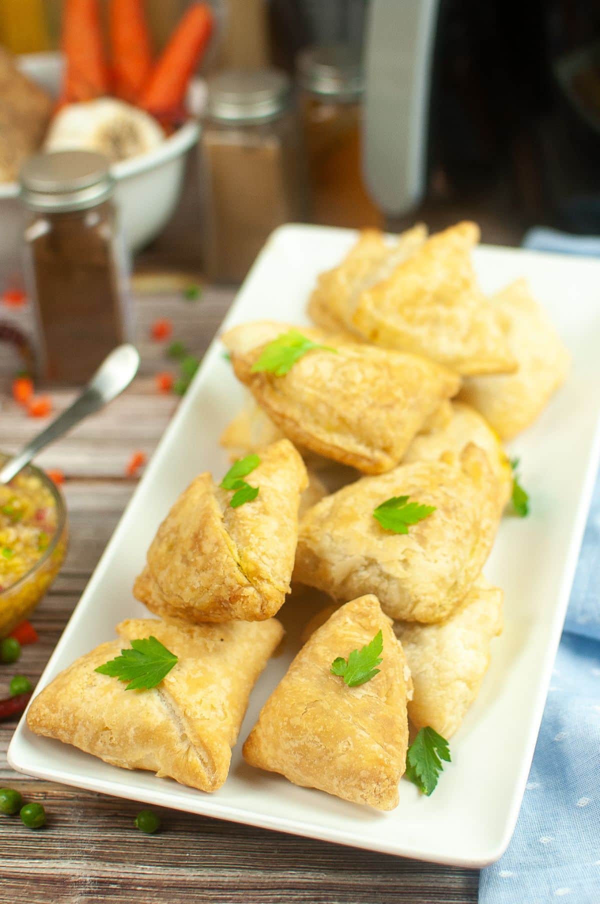 Air Fryer Samosas on a serving plate, garnished with parsley. chutney, spices, Air Fryer on the side.