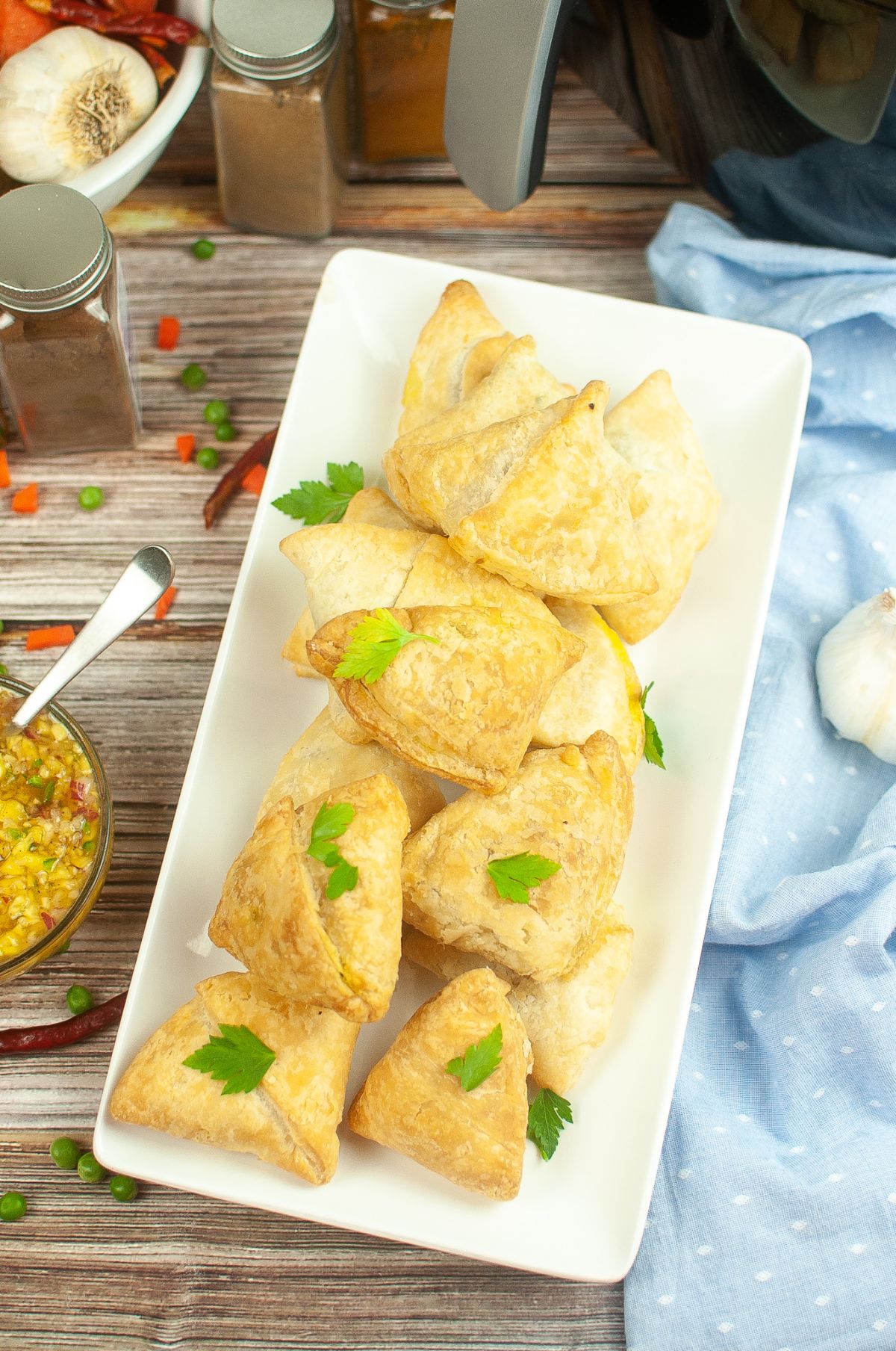 Air Fryer Samosas on a serving plate, garnished with parsley. chutney, spices, Air Fryer on the side.