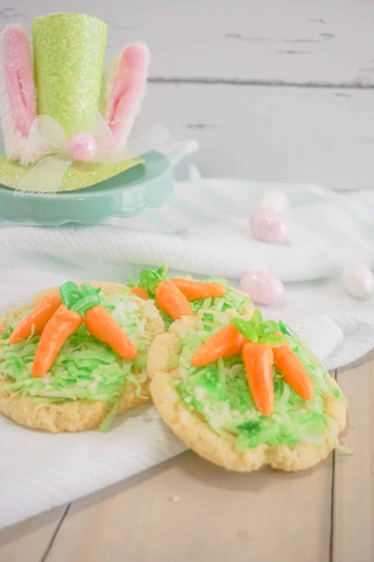 Carrot Sugar Cookies on a white cloth, bunny hat and egg candies on the side.