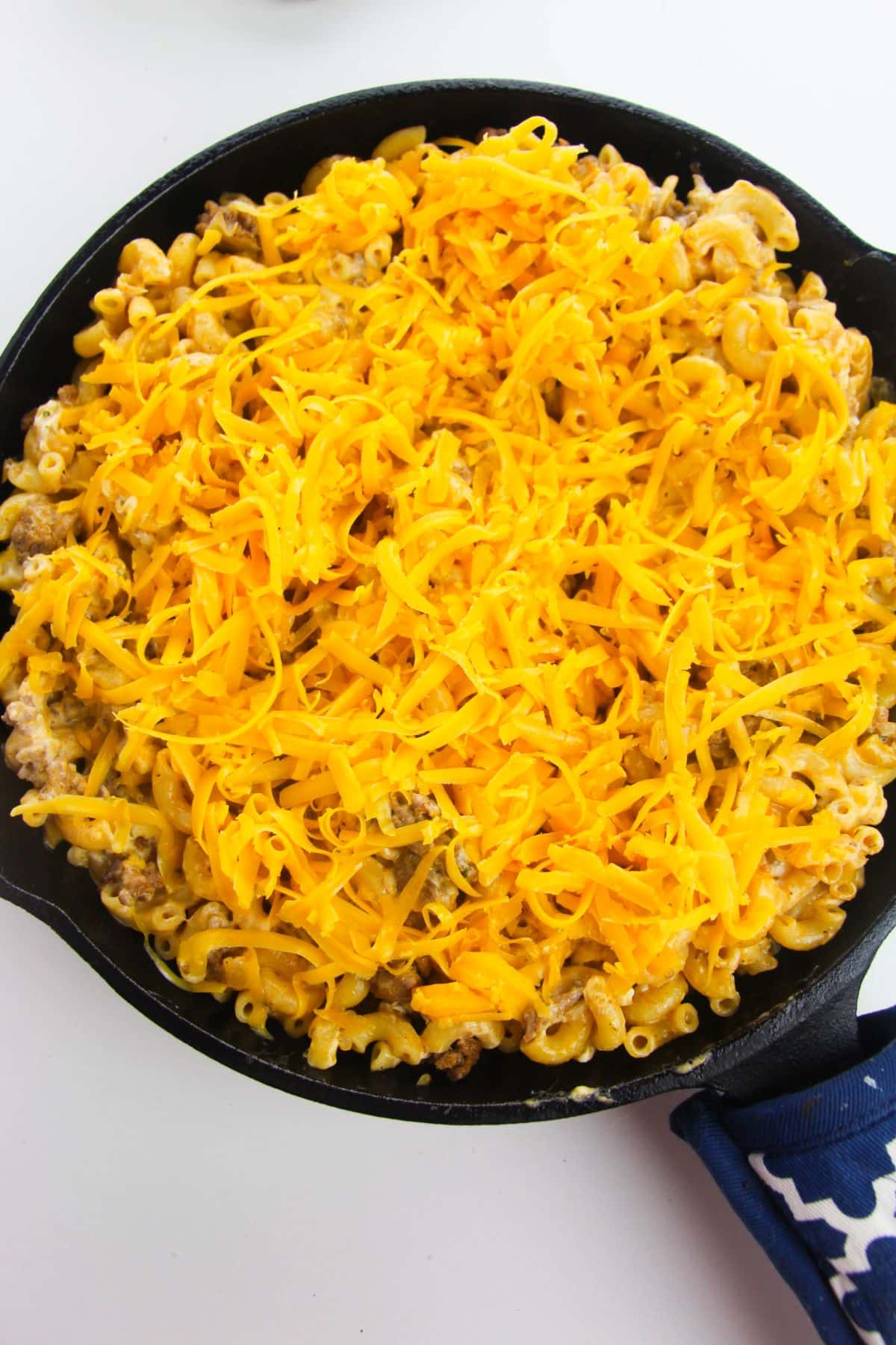 Shredded cheddar cheese is added to the pasta mixture in a large skillet.