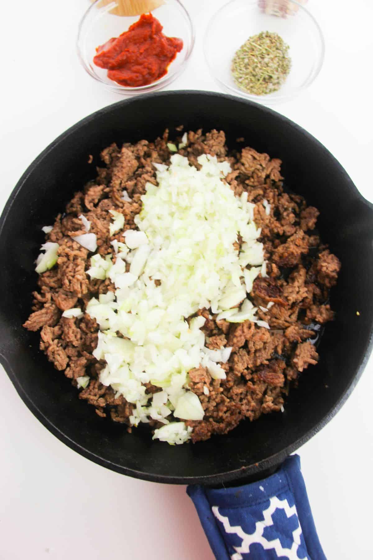 Onions are added in a large skillet with ground beef.