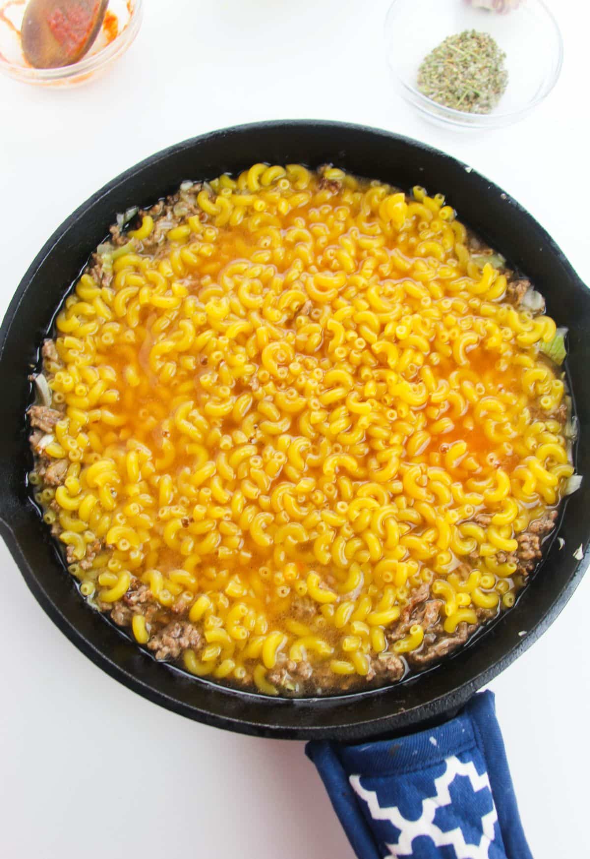 tomato paste, broth, uncooked pasta are added into the skillet.