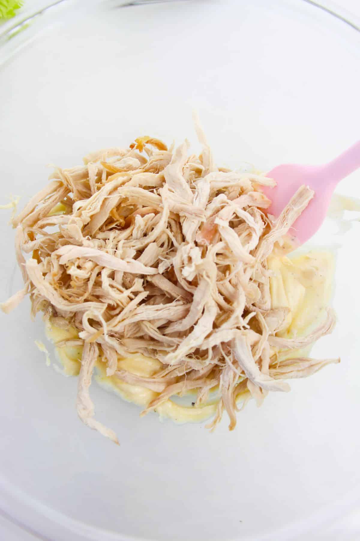 shredded chicken is added to the mixture in a large bowl with pink spatula.