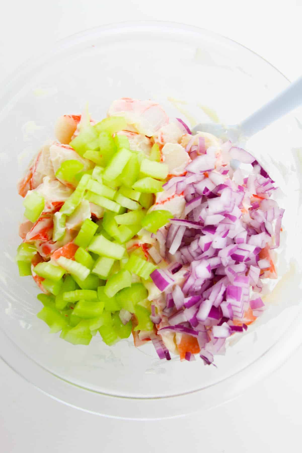 diced red onion and celery are added to the crab mixture. spatula on the side.