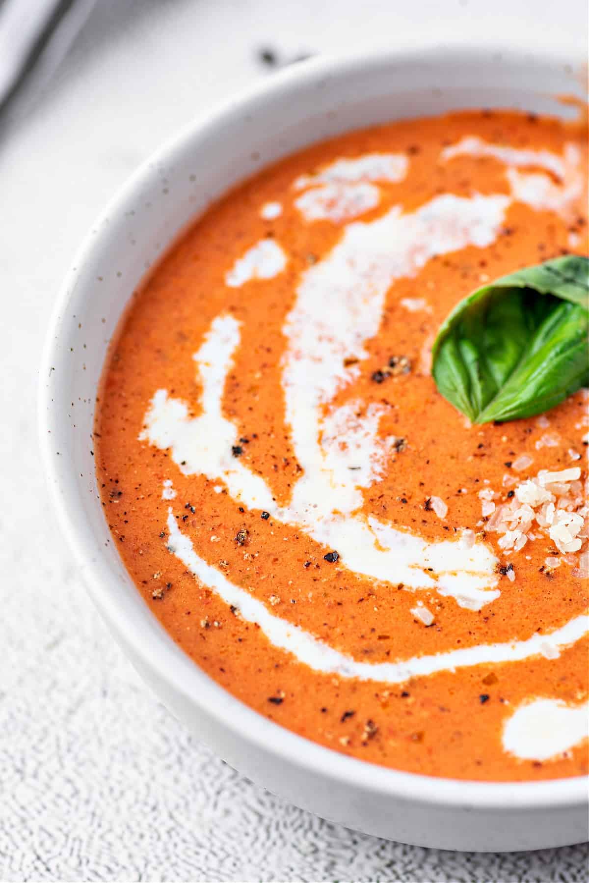 Creamy Keto Tomato Soup in a serving bowl, garnished with basil, black pepper and heavy cream.
