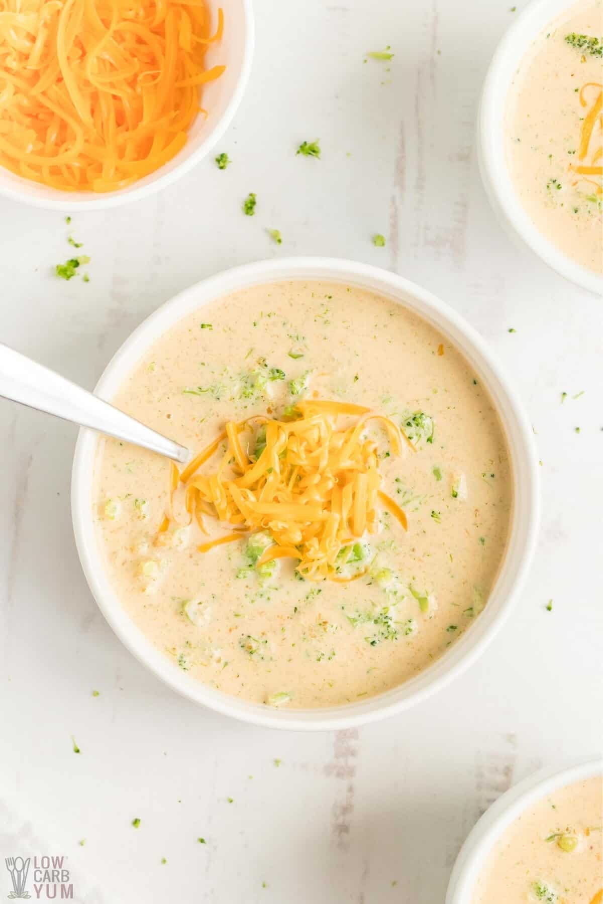 Low Carb Broccoli Cheese Soup in a serving bowl with a spoon and shredded cheese. 