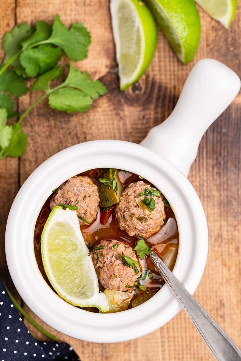 Keto Albondigas Meatball Soup in a serving bowl with spoon. garnished with lime and cilantro. 