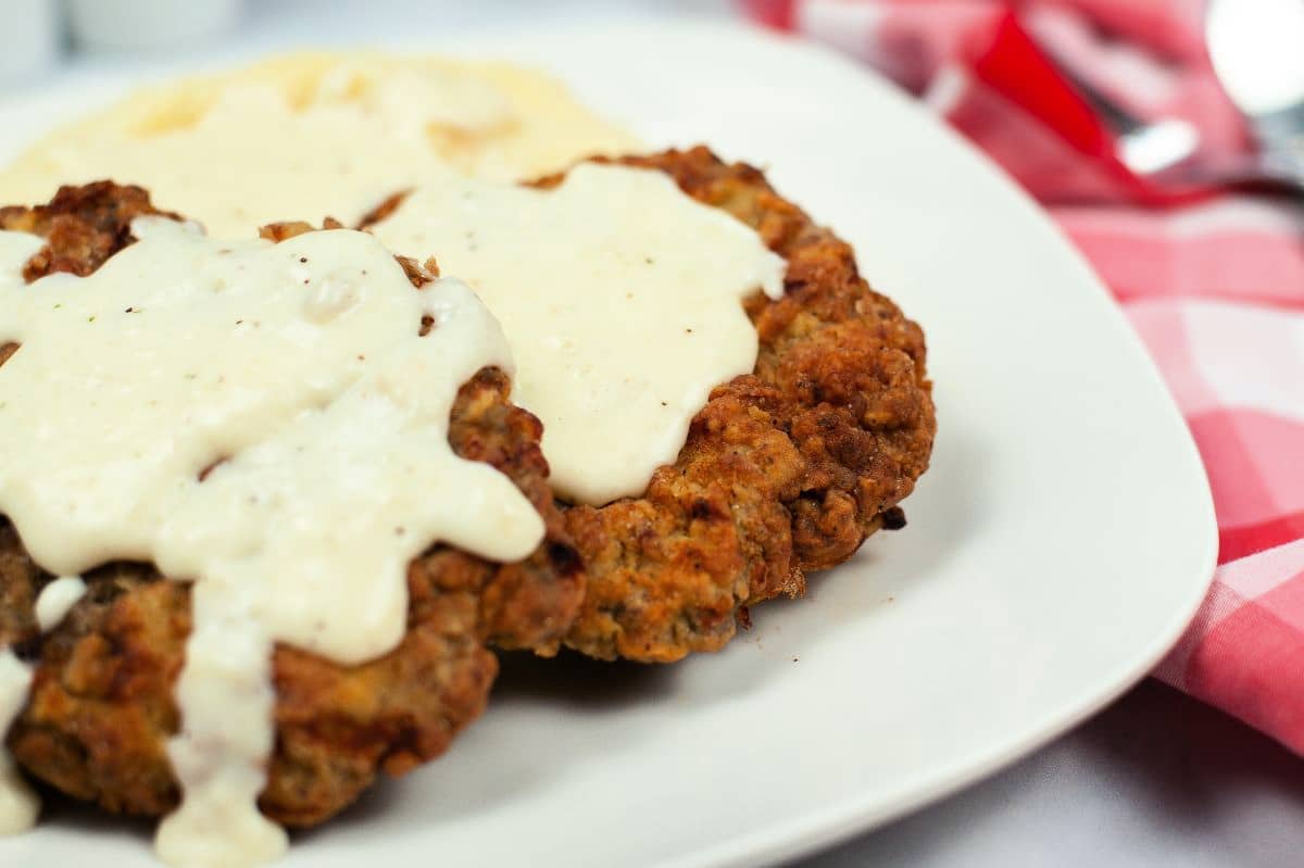 close up of chicken fried steak with gravy on a white plate 