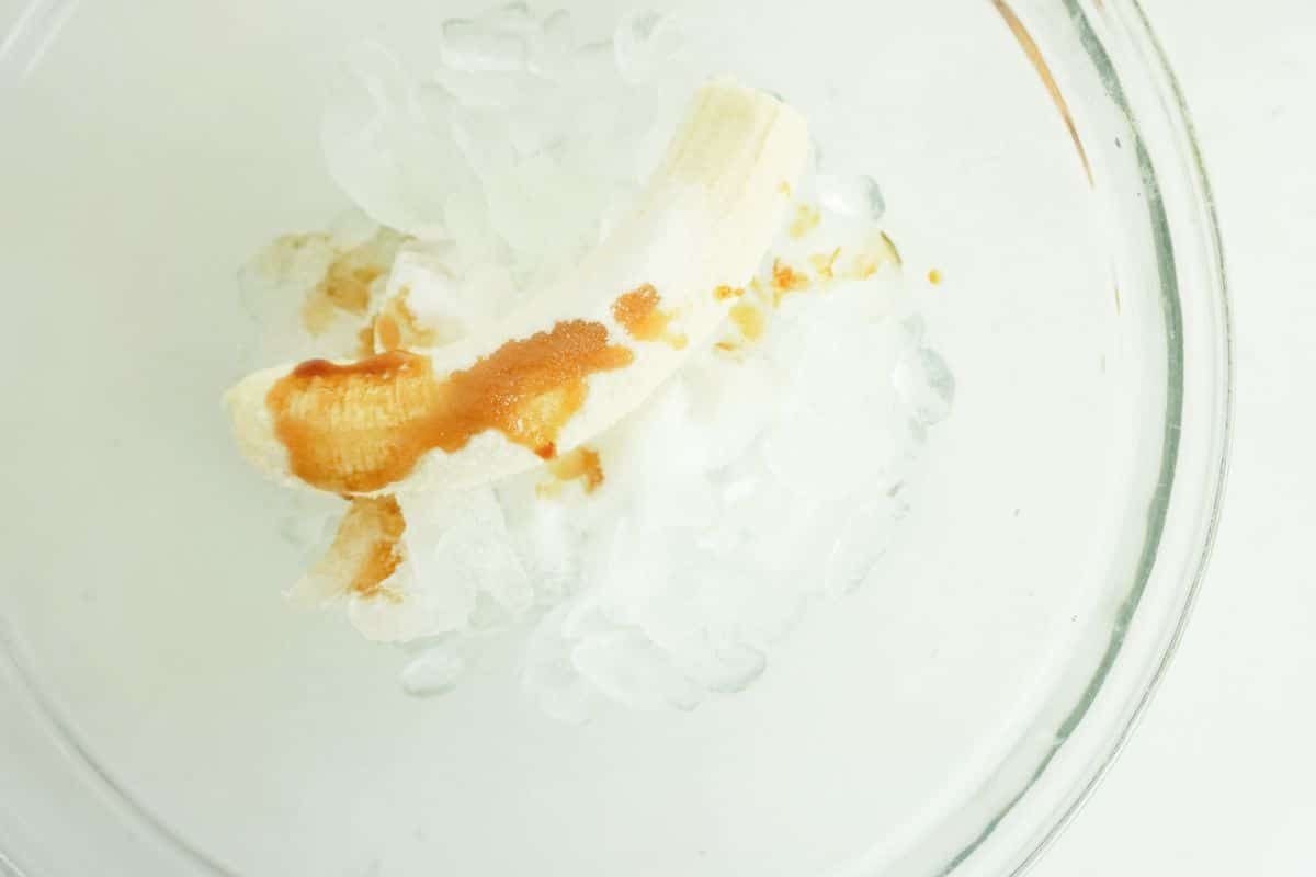 ice, banana, coconut cream mixture and vanilla extract in a glass bowl.
