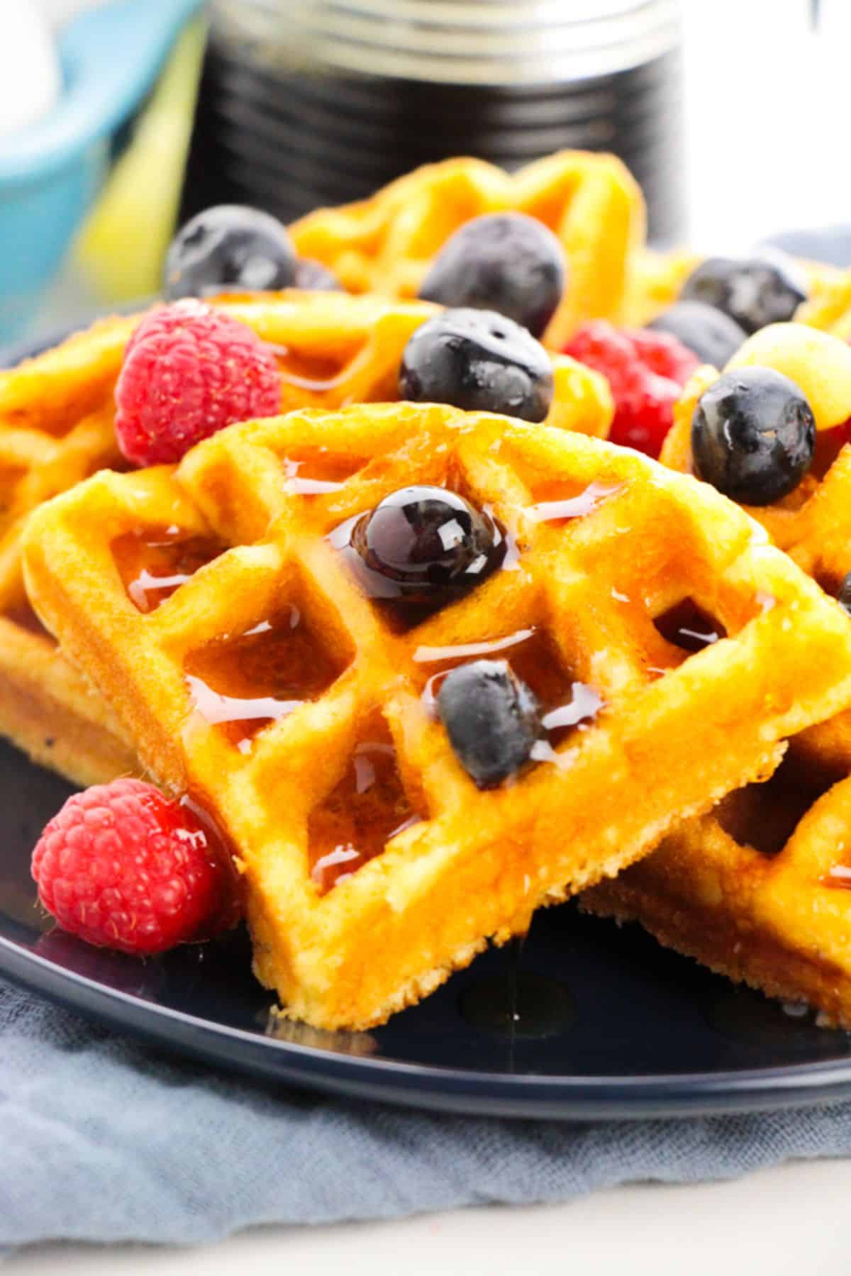 Cake Mix Waffles on a serving plate, garnished with maple syrup and berries.