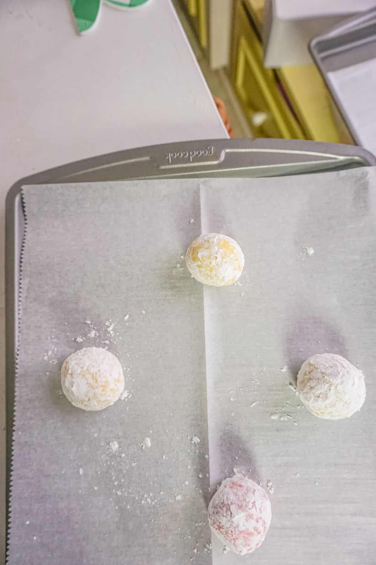 cookie dough balls with powdered sugar on a baking pan.