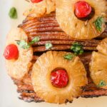 Close-up of a ham with pineapple and cherries, topped with maraschino cherries and garnished with parsley.