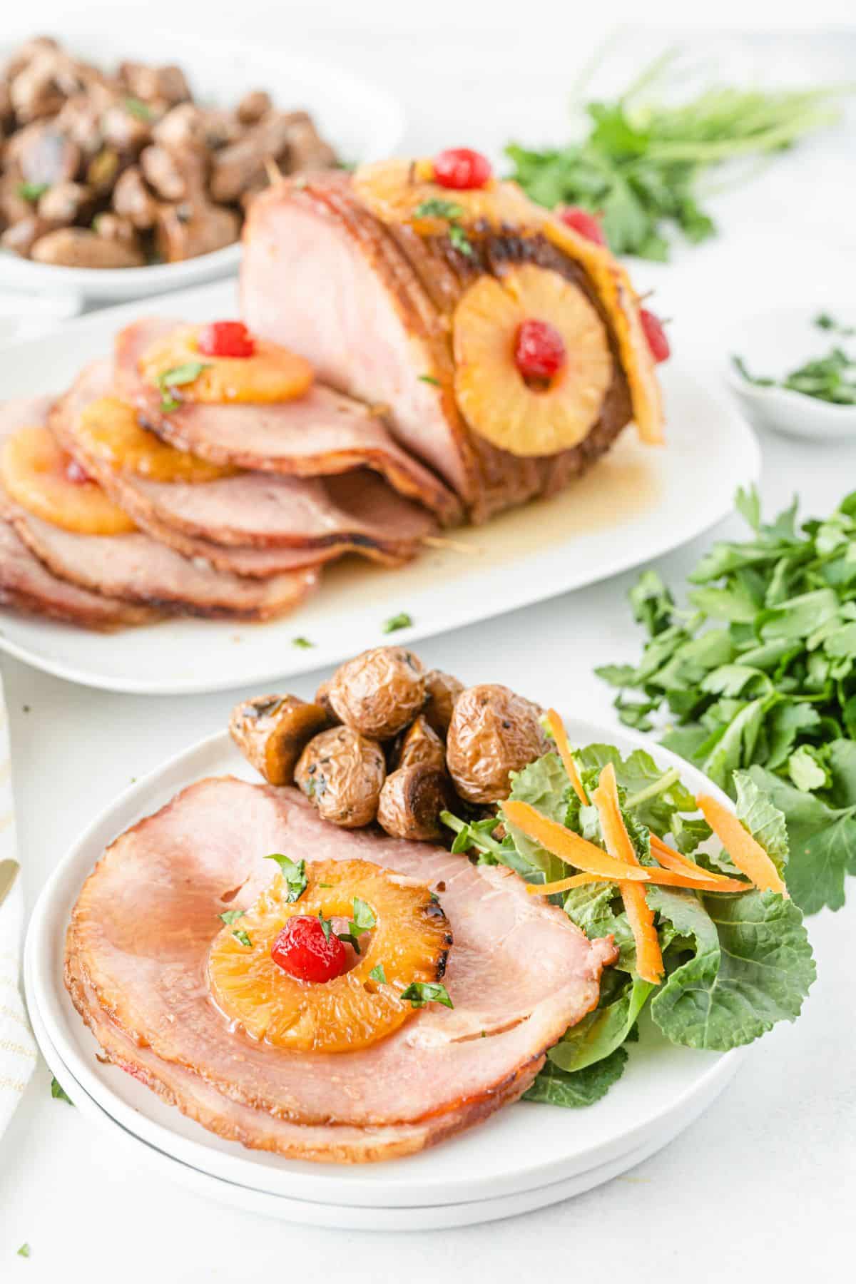 Baked ham with cherries and pineapples on a serving plate, with baby potatoes on the side.