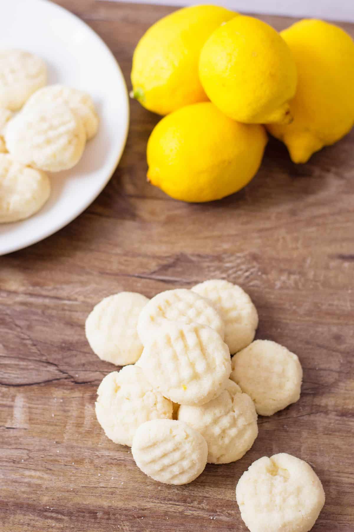 Lemon Shortbread Cookies on a wooden table. Lemon and a plate with cookies on the side.