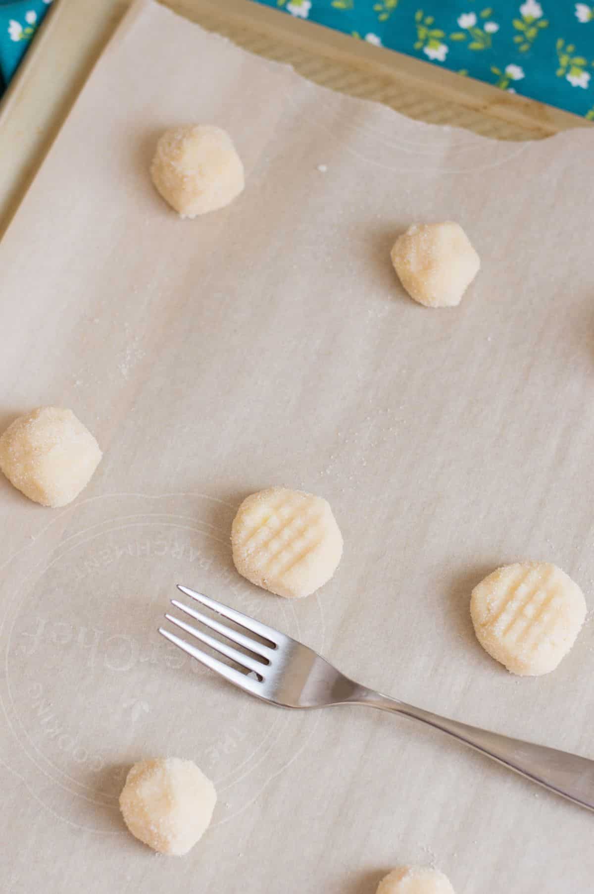 dough balls are being flattened using a fork on parchment paper on a cookie sheet.