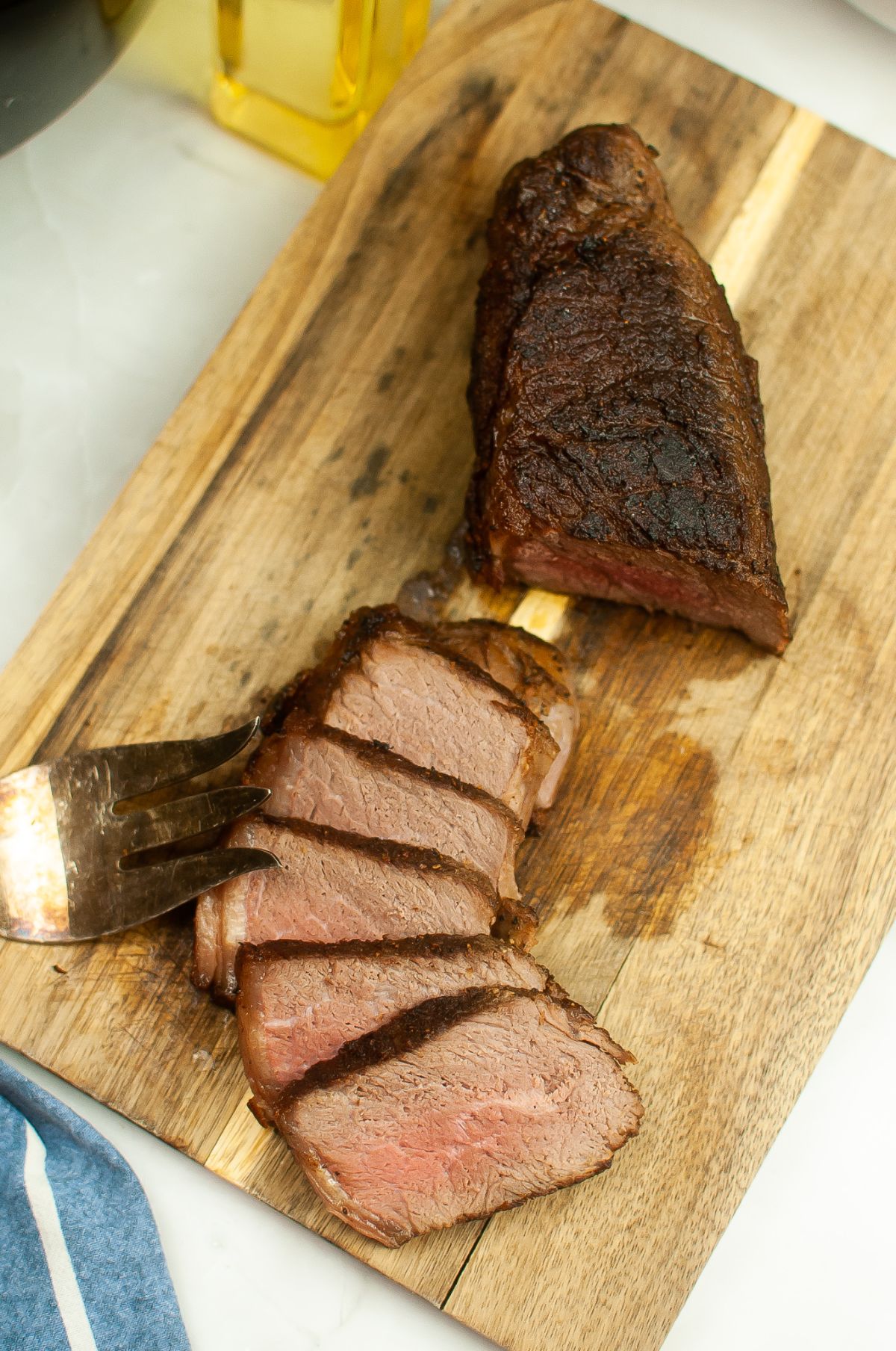 Sliced beef roast on a wooden chopping board with serving fork on the side.