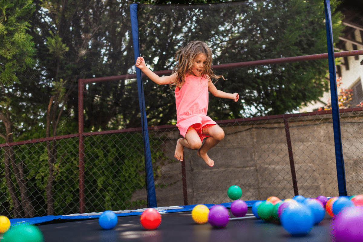 a girl jumping on a trampoline surrounded by colorful soft balls.