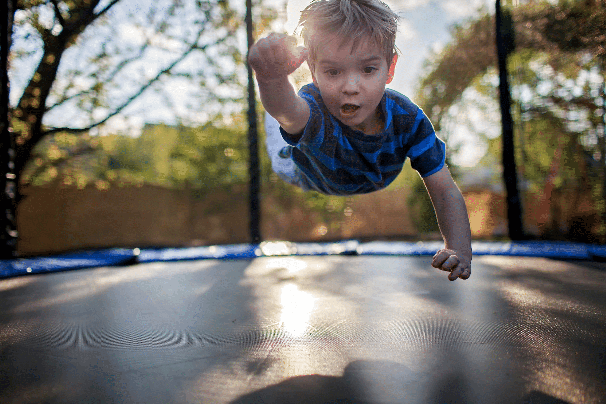 a boy is jumping on a trampoline while stretching out his arm.