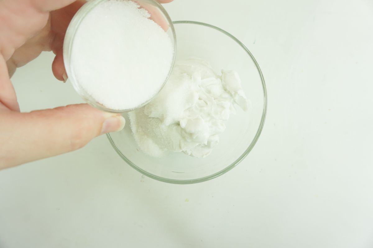 pouring the sugar into a glass bowl with coconut cream in it.