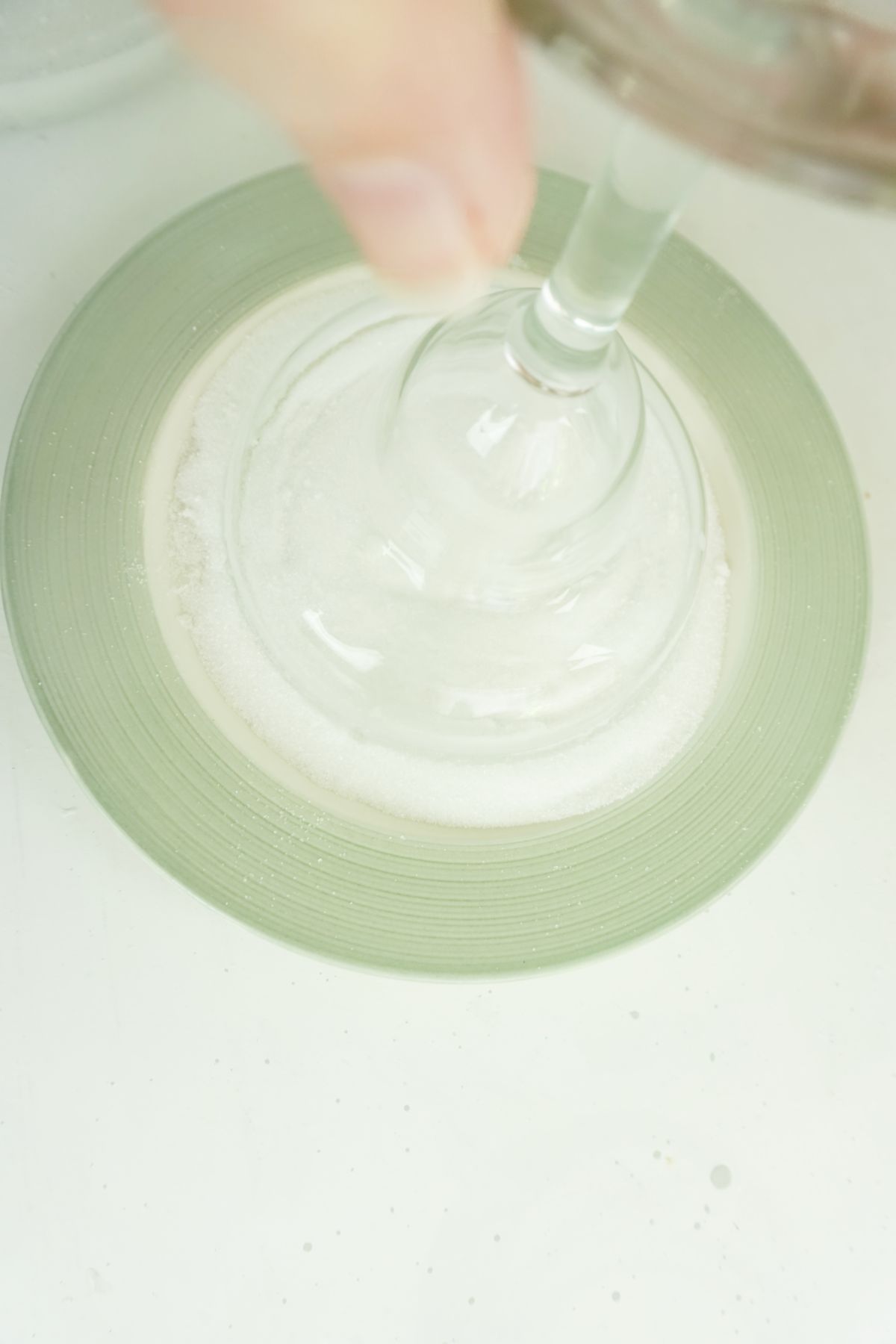 a hand dipping an upside down glass on a plate with sugar.