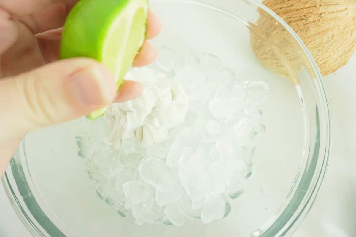 pouring the lime juice into a glass bowl with ice and coconut cream in it.