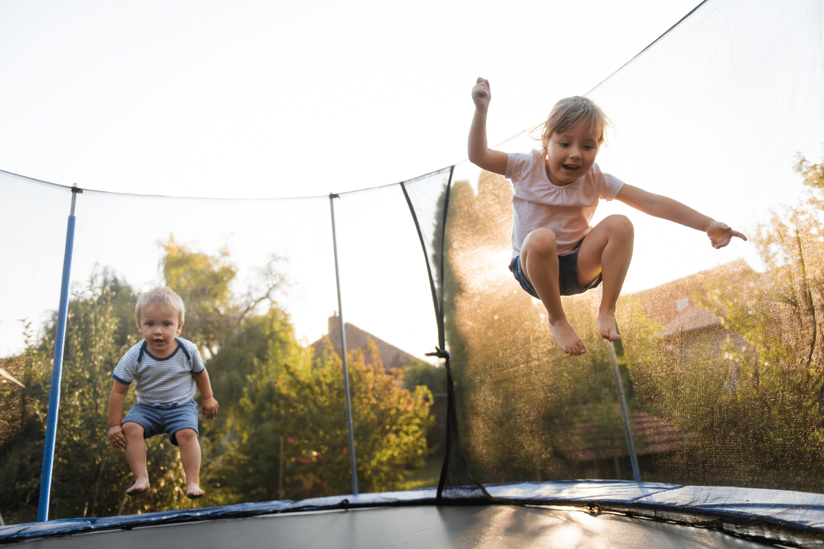 Two kids are jumping on a trampoline.