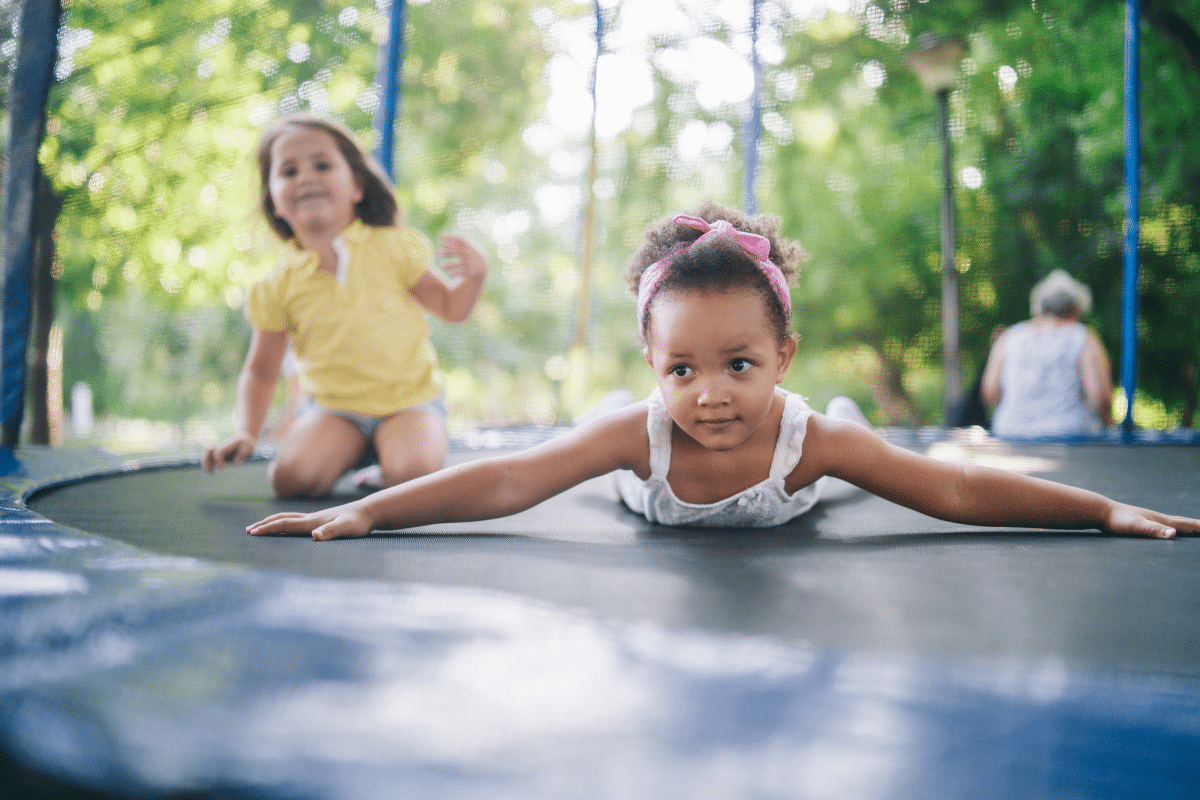 two young girls are sitting and lying down on a trampoline.