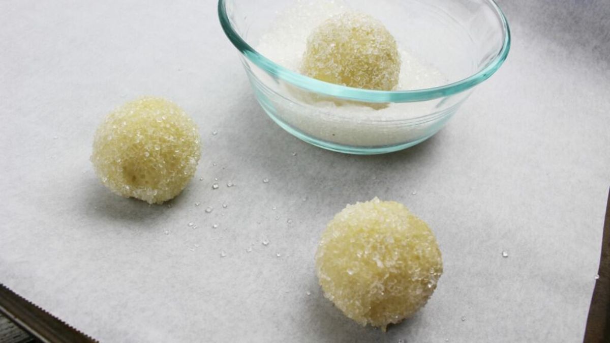 cookie dough balls coated in sugar crystals are placed on cookie sheet lined with parchment paper.