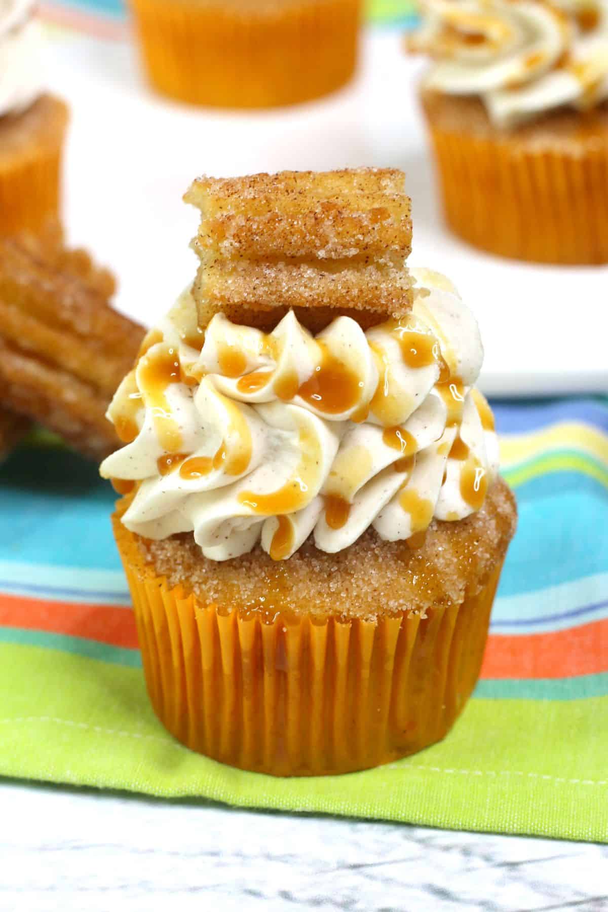 Cinnamon Cupcake on a colorful tablecloth, garnished with caramel sauce and a piece of churro.