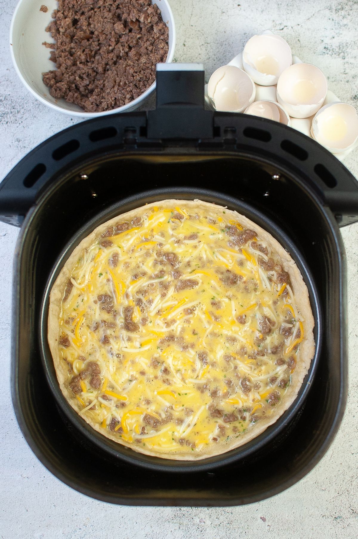 Pan with pie crust filled with sausage, egg and cheese inside the Air Fryer.