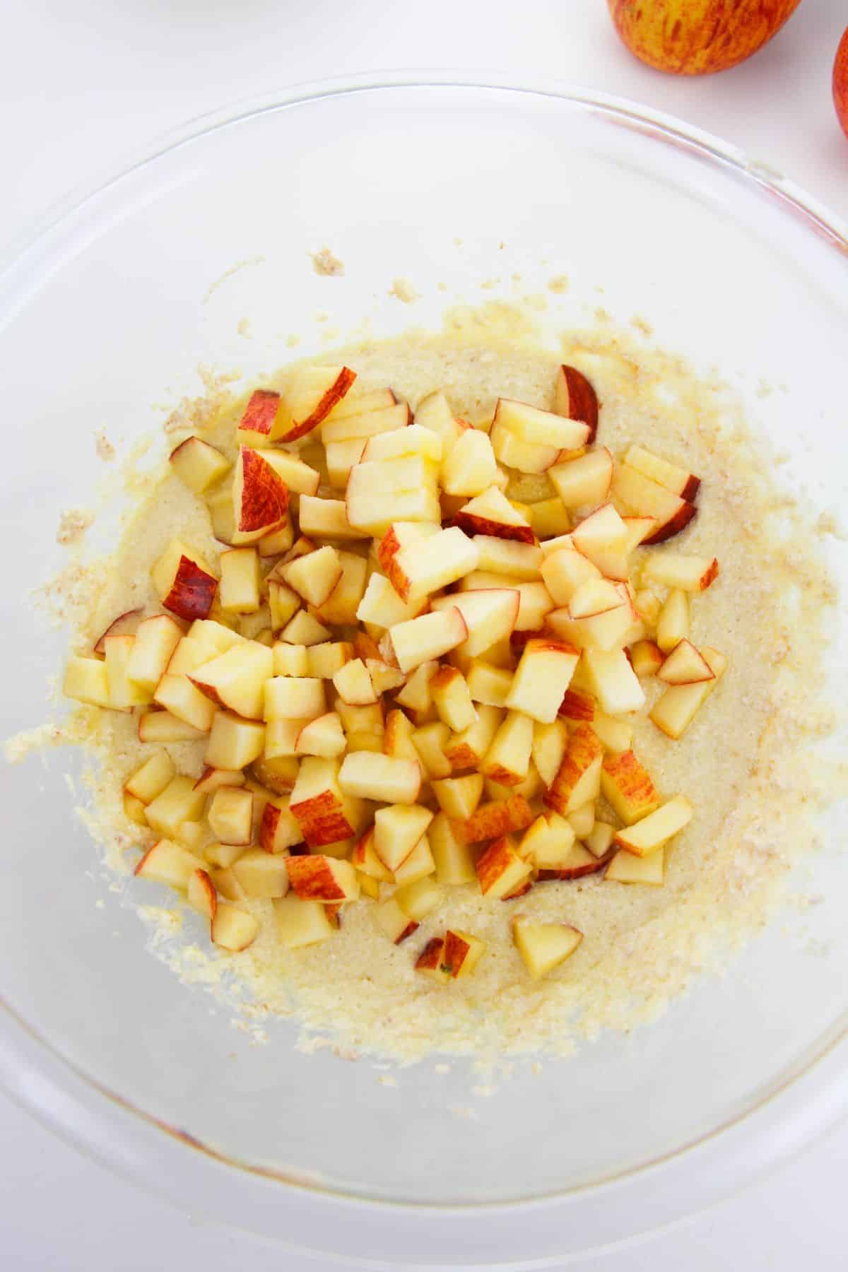 chopped apples are added to the batter in a mixing bowl.