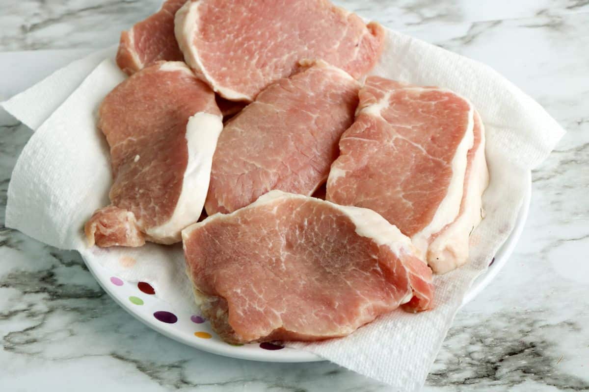 Raw porkchops on a plate with a paper towel.