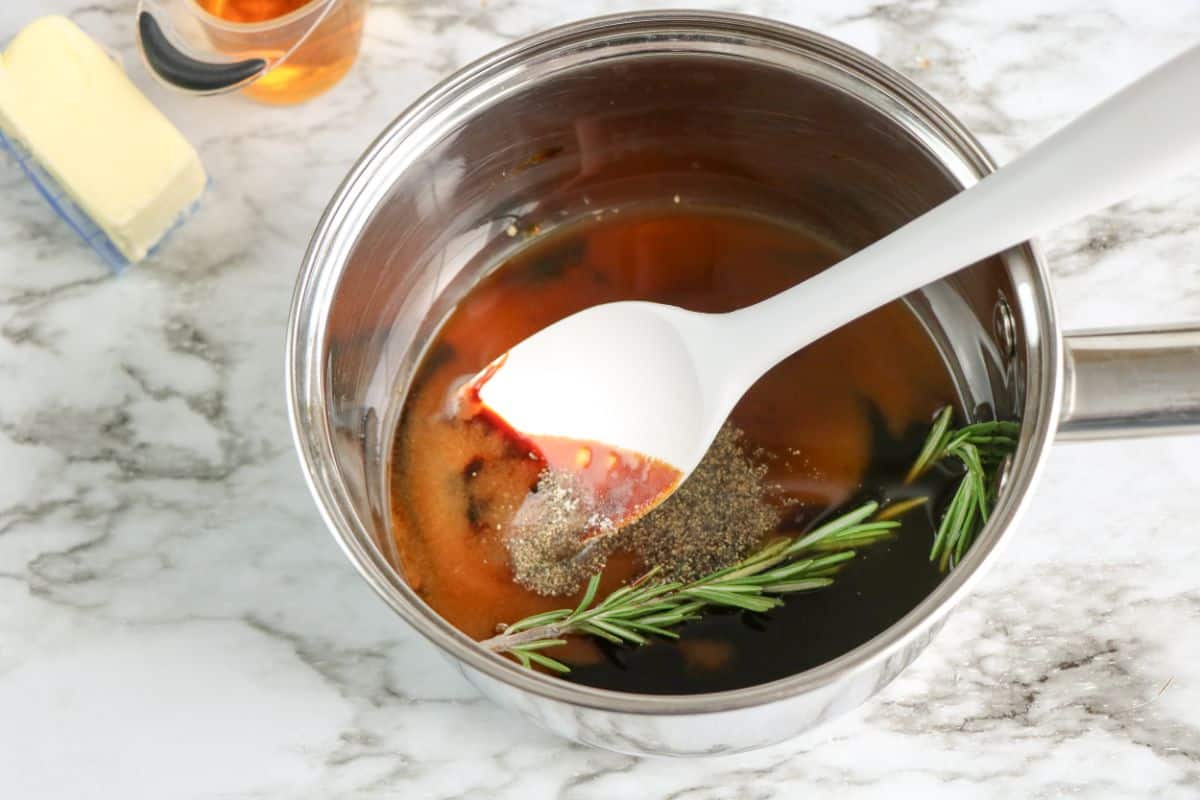 Molasses, apple cider vinegar, and rosemary in a small sauce pan with white spoon in it.