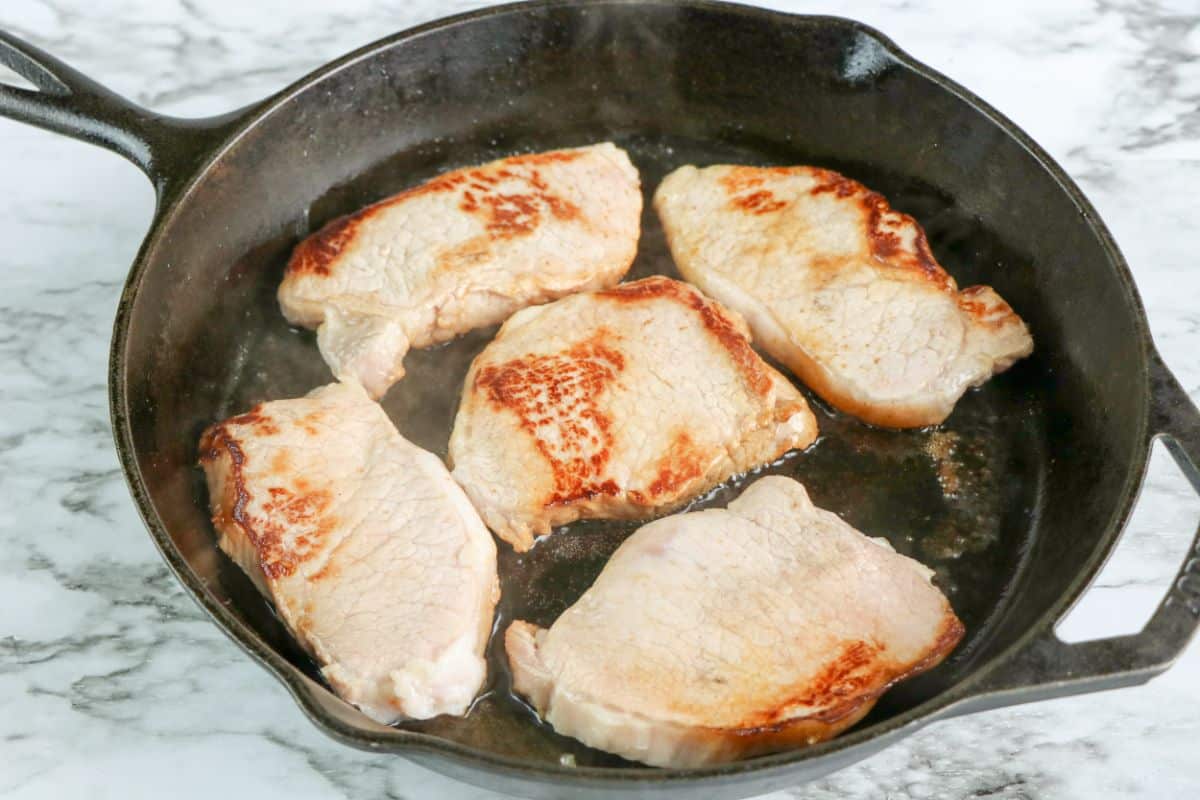 Pork chops cooking in a large skillet.