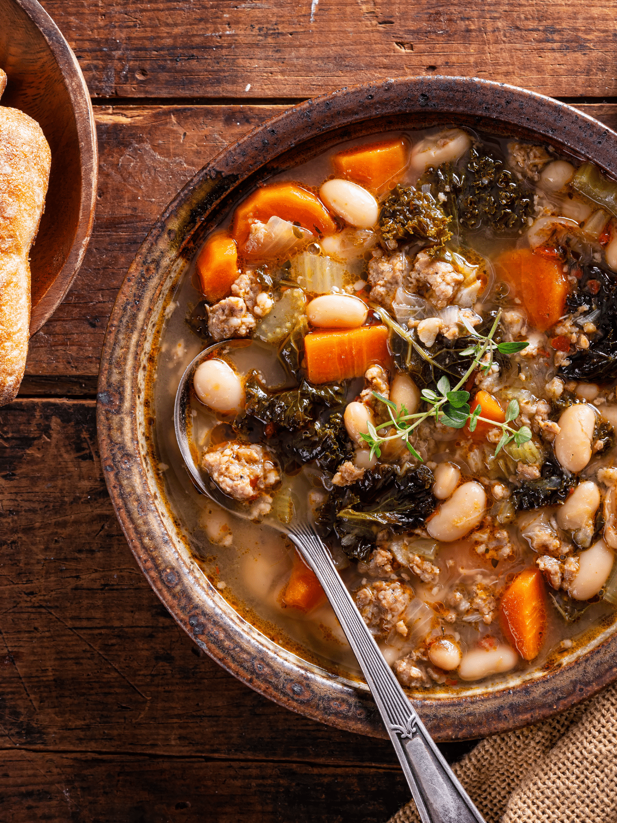 Sausage, kale and white cannellini beans soup in a brown bowl, with spoon in it.