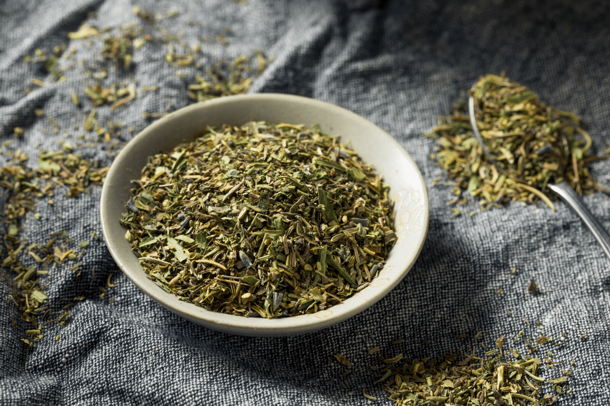 Herbes de Provence in a bowl with a spoon full of herbs on the side.
