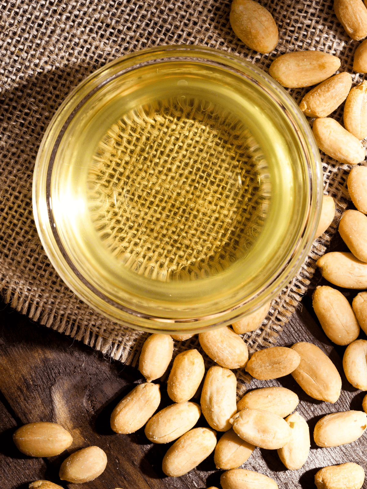 A small bowl of peanut oil sits on a rustic sack with peanuts on the side.