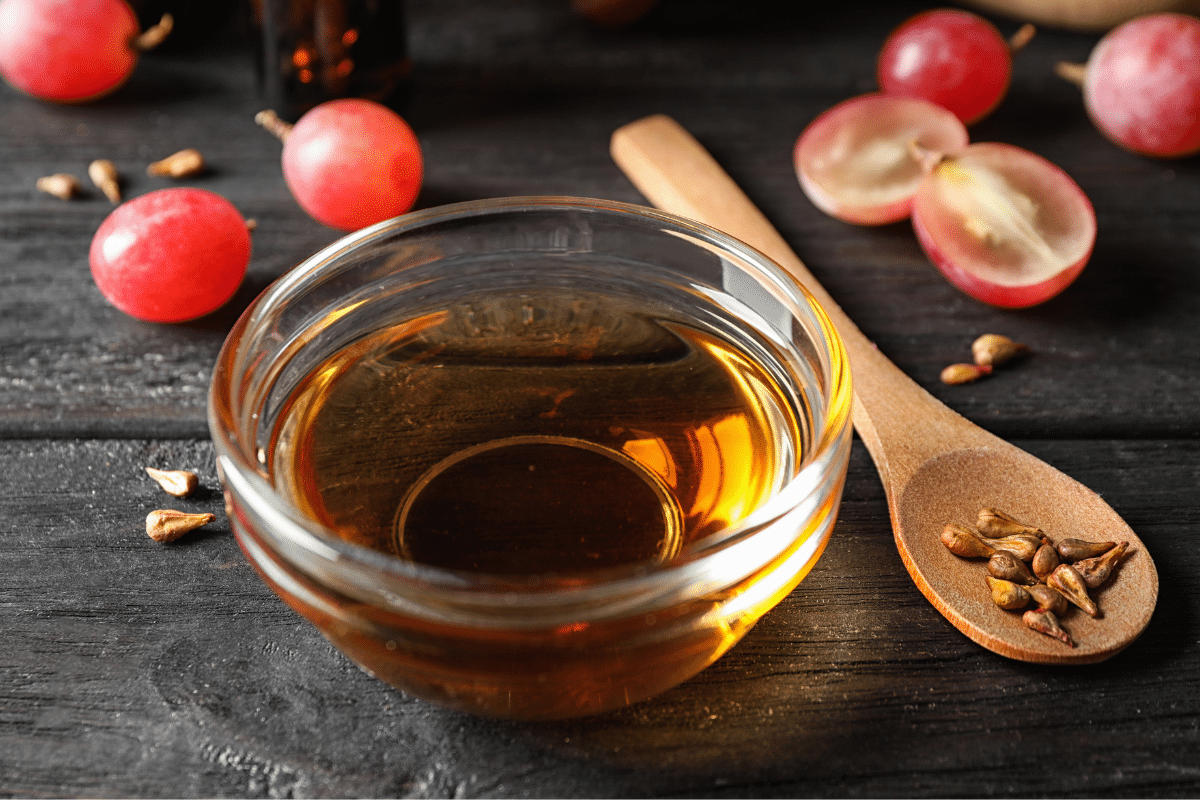 Grapeseed oil in a small bowl, grapes and grapeseed on a wooden spoon on the side.